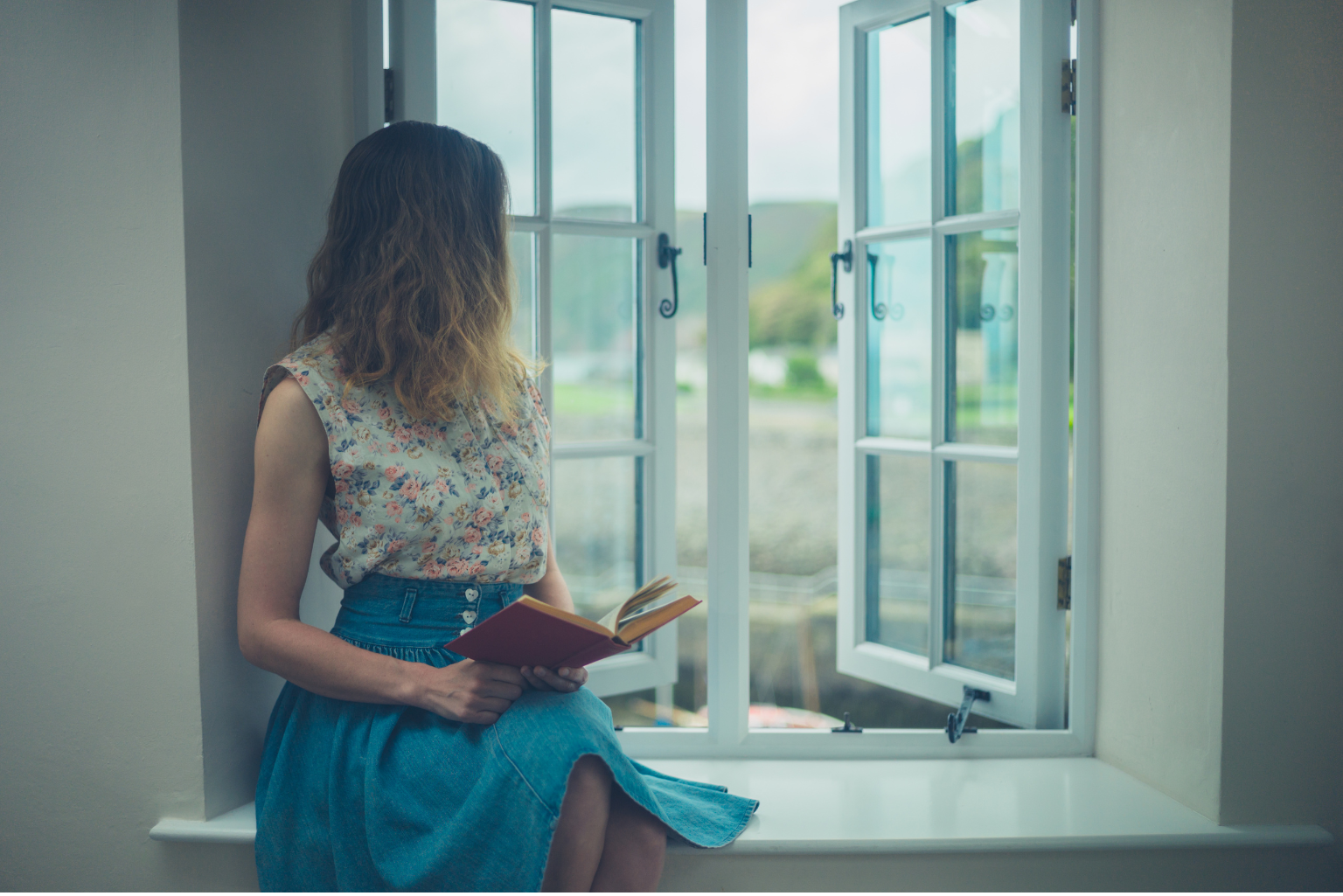 a woman sitting on a window sill reading a book.